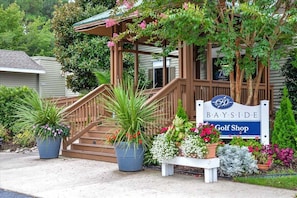 A wooden porch with a sign reading 'BAYSIDE Golf Shop,' surrounded by potted plants and a staircase. - New Listing: Bayside Resort Fenwick Island at The Point - Luxury (Selbyville)