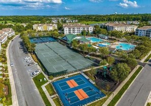 An aerial view of a residential area with a tennis court, swimming pool, and multiple apartment buildings.