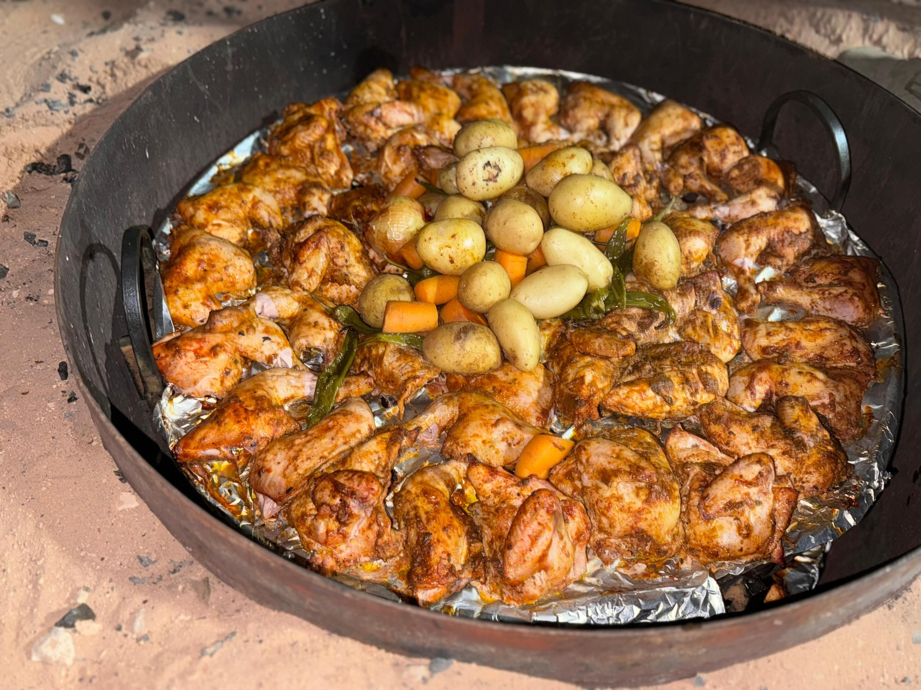 A large, round, metal cooking pan filled with roasted chicken and vegetables.