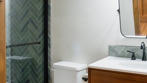 A modern bathroom with a white toilet, wooden vanity, and a glass shower enclosure. - Luxury villa w/ lake+mtn views+private theatre! (Grand Lake)
