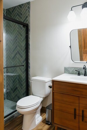 A modern bathroom with a white toilet, wooden vanity, and a glass shower enclosure. - Luxury villa w/ lake+mtn views+private theatre! (Grand Lake)
