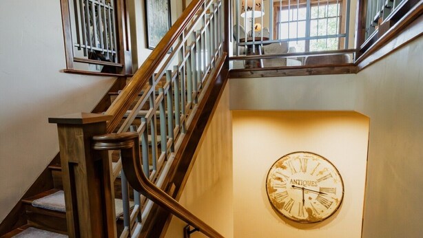 A staircase with wooden railings and a wall-mounted clock labeled 'ANTIQUES.' - Luxury villa w/ lake+mtn views+private theatre! (Grand Lake)