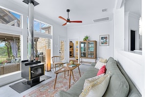 Cozy living space with a fireplace, wicker sofa, and large windows offering a view of the outdoors.