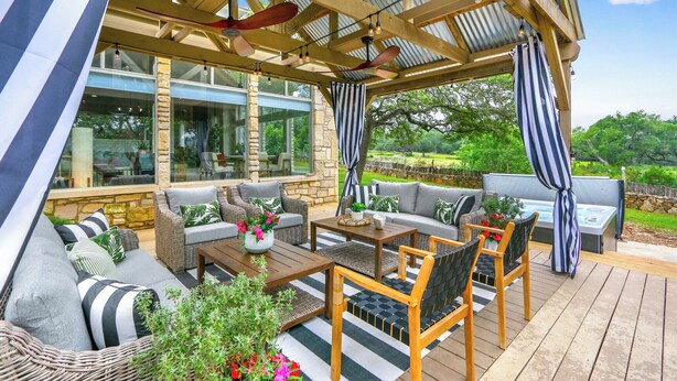 A covered outdoor seating area with wicker furniture, a wooden table, and a hot tub. - Hidden Hills I Family Vacation, Hot tub, Sleeps 24, 56 scenic acres for hiking! (Fischer)