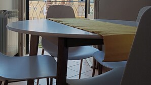 A balcony with a table and chairs, a view of palm trees, and a building in the background.