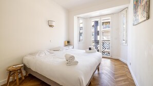 Une chambre spacieuse avec un grand lit, un tabouret en bois et une vue sur un balcon extérieur.