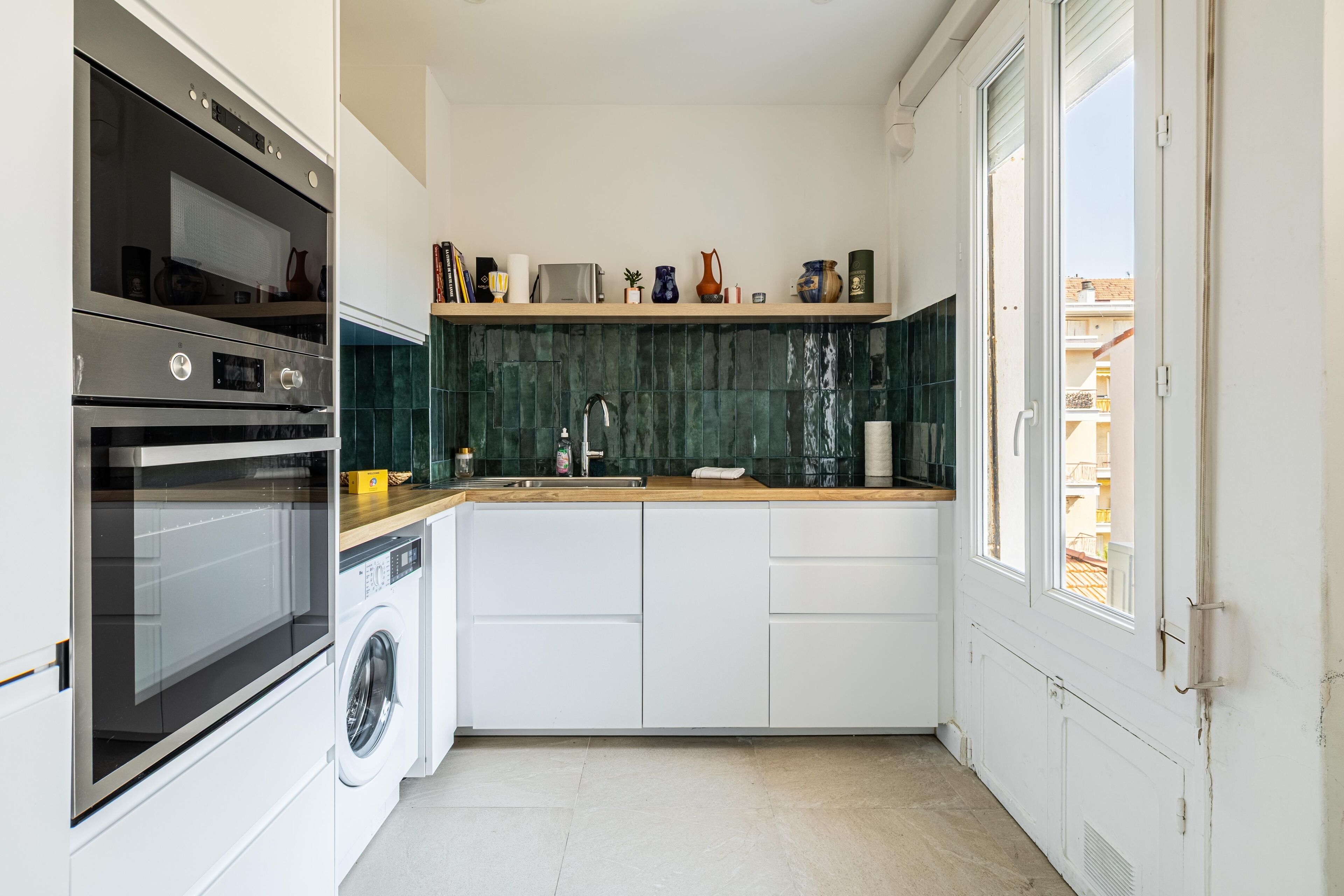 Cozinha compacta com eletrodomésticos embutidos, máquina de lavar e janela com vista para o exterior.