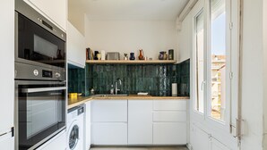 Une cuisine compacte dotée d’appareils électroménagers intégrés, d’un lave-linge et d’une fenêtre donnant sur l’extérieur.