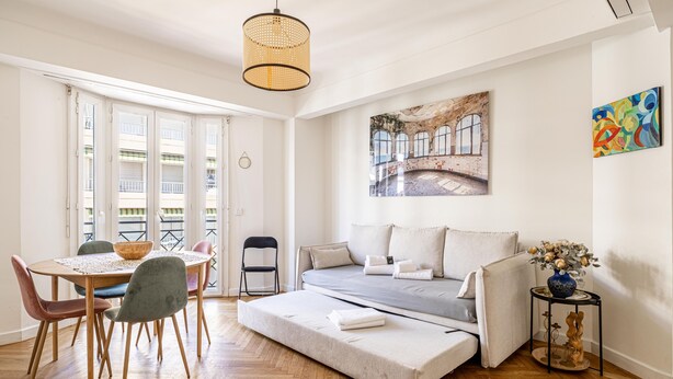 Une chambre moderne avec un lit, une table à manger et des chaises, une petite table d’appoint et un tableau au mur.