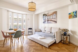 Une chambre moderne avec un lit, une table à manger et des chaises, une petite table d’appoint et un tableau au mur.