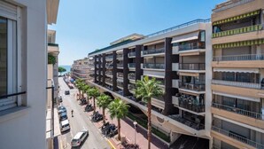 Un immeuble résidentiel à plusieurs étages doté de balcons, une rue bordée de voitures garées et des palmiers.