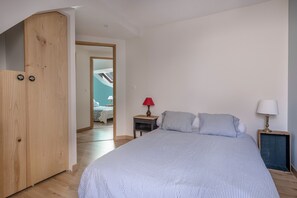 A bedroom with a large bed, a wooden wardrobe, a small bedside table with a lamp, and a view into another room. - 500m Libraires beach - Pornichet (Pornichet)