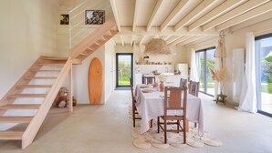 Un vaste espace dédié à la salle à manger, agrémenté d’un escalier en bois, d’une planche de surf et offrant une vue sur l’extérieur.