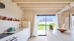 Une cuisine moderne avec des meubles blancs, un plan de travail noir et une vue sur l’extérieur grâce à une porte-fenêtre coulissante.