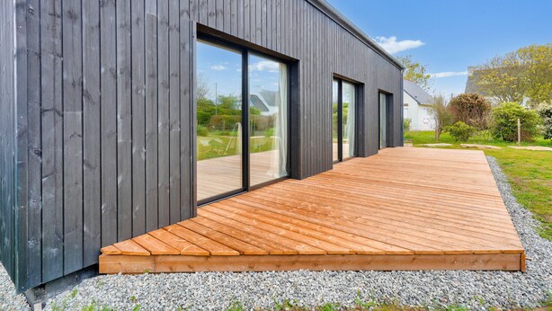 Un bâtiment moderne doté de grandes fenêtres et d’une terrasse en bois.