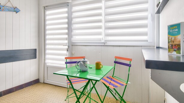 A small room with a green table and colorful chairs, a window with blinds, and a sign on the wall.