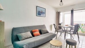 A modern living room with a grey sofa, a small round table, and a dining area with chairs and a table.