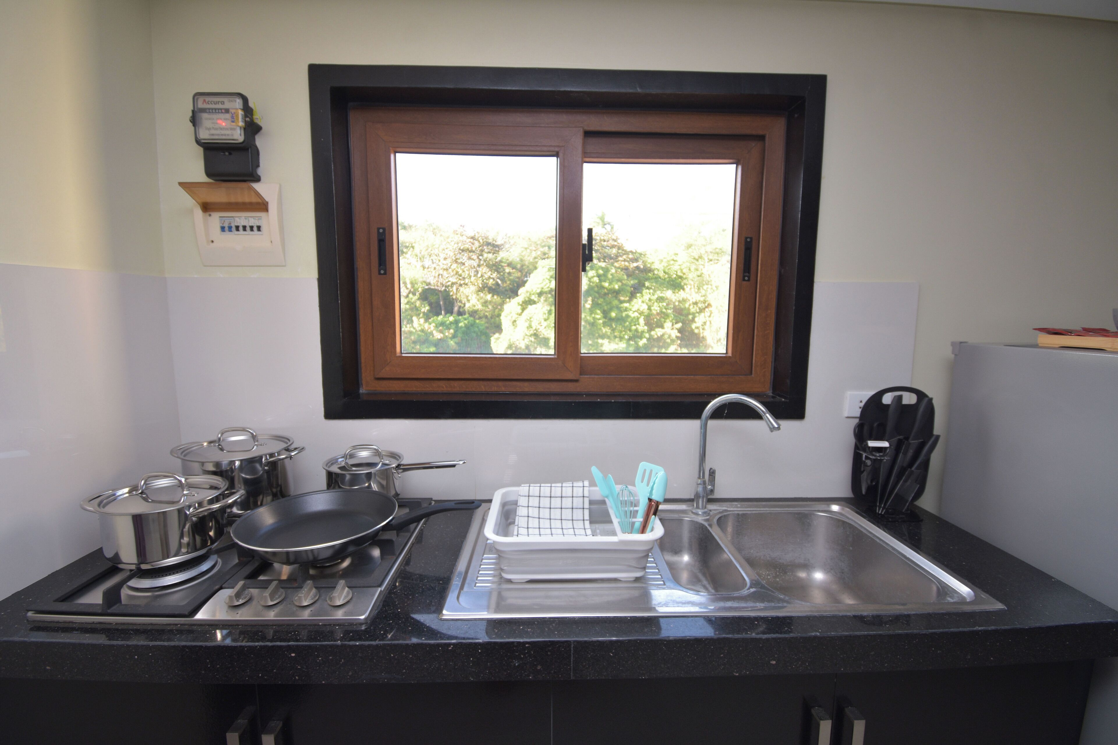Una cocina con ventana, estufa, lavaplatos y diferentes ollas y sartenes.