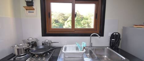 Una cocina con ventana, estufa, lavaplatos y diferentes ollas y sartenes.