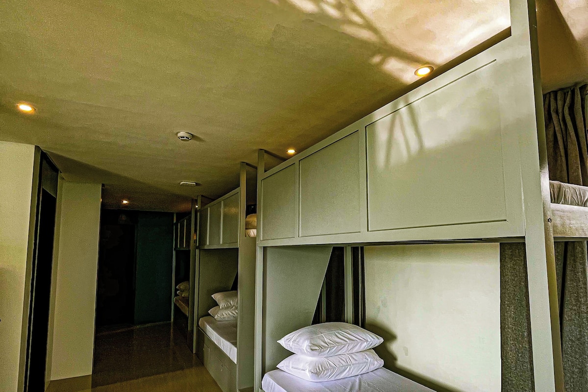 Un couloir étroit avec des lits superposés, un plancher en bois et une porte donnant sur une autre pièce.