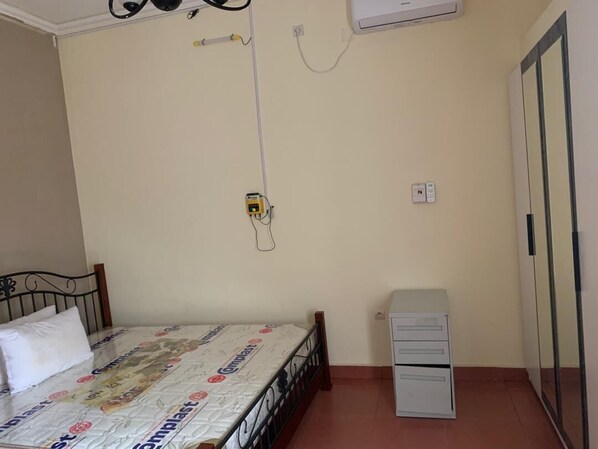 Un dormitorio con cama, mesita de noche, aire acondicionado, toma de corriente y armario.