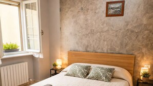 A bedroom with a large bed, a radiator, a window with plants, and a textured wall. - Kidonia Mountain – Fresh Air, Lake Views, Authentic Village Life (Zone)