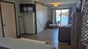 Een kamer met een bed, een stoel, een televisie, een schuifdeur en uitzicht op het omliggende landschap.