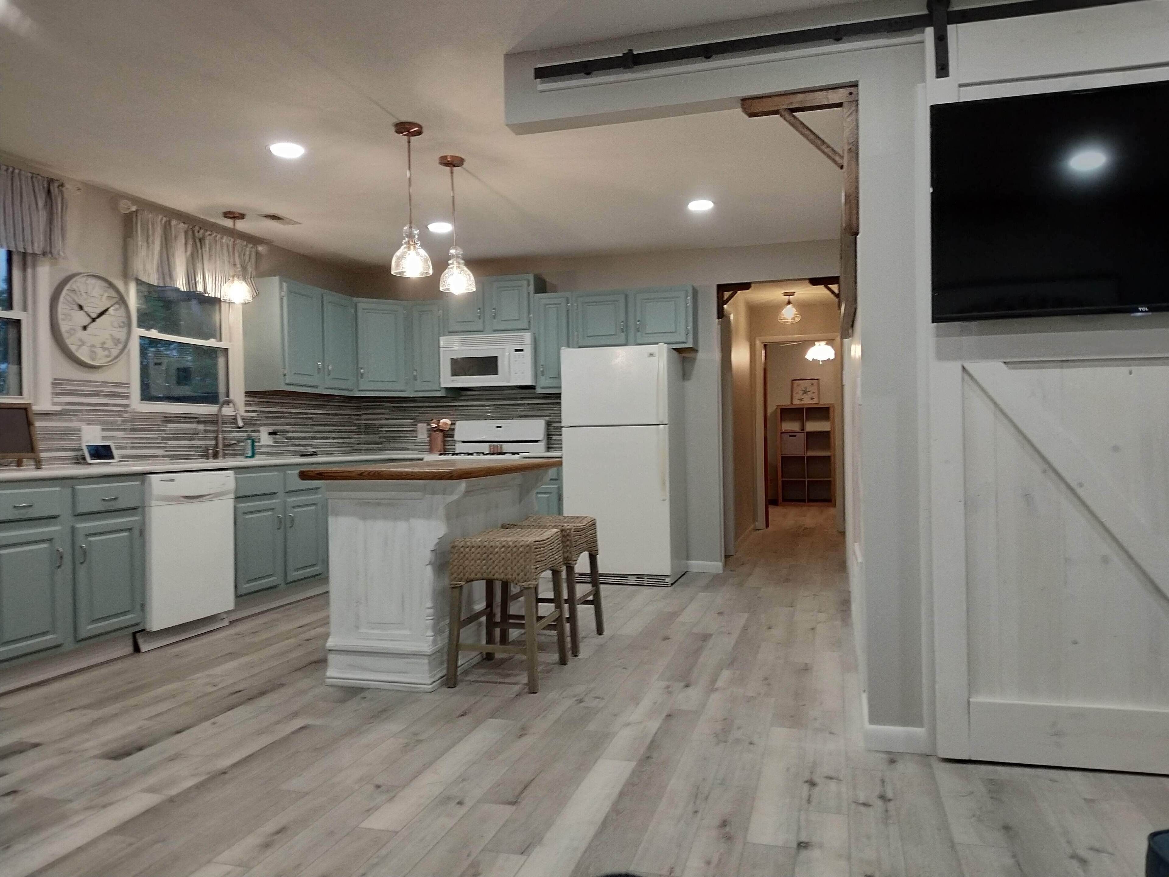 Una cocina con armarios azul claro, una isla blanca con taburetes, un microondas y un refrigerador.