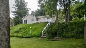 Een huis met een wenteltrap die naar de voordeur leidt, omringd door weelderige begroeiing en bomen.