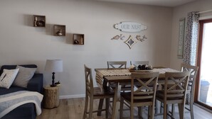 Een gezellige woonkamer met een donkerblauwe bank, een houten salontafel met decoratieve objecten, en een eethoek met houten stoelen en een tafel.