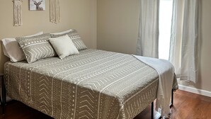Une chambre avec un grand lit, un plancher en bois et une fenêtre avec des rideaux.