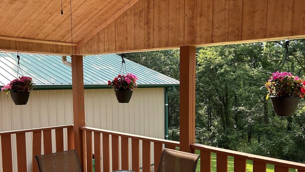 Une terrasse couverte avec une table et des chaises en verre, un ventilateur de plafond et des jardinières suspendues.