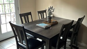 Une salle à manger avec une table en bois foncé, six chaises, une plante en pot et un panneau indiquant « Famille » accroché au mur.