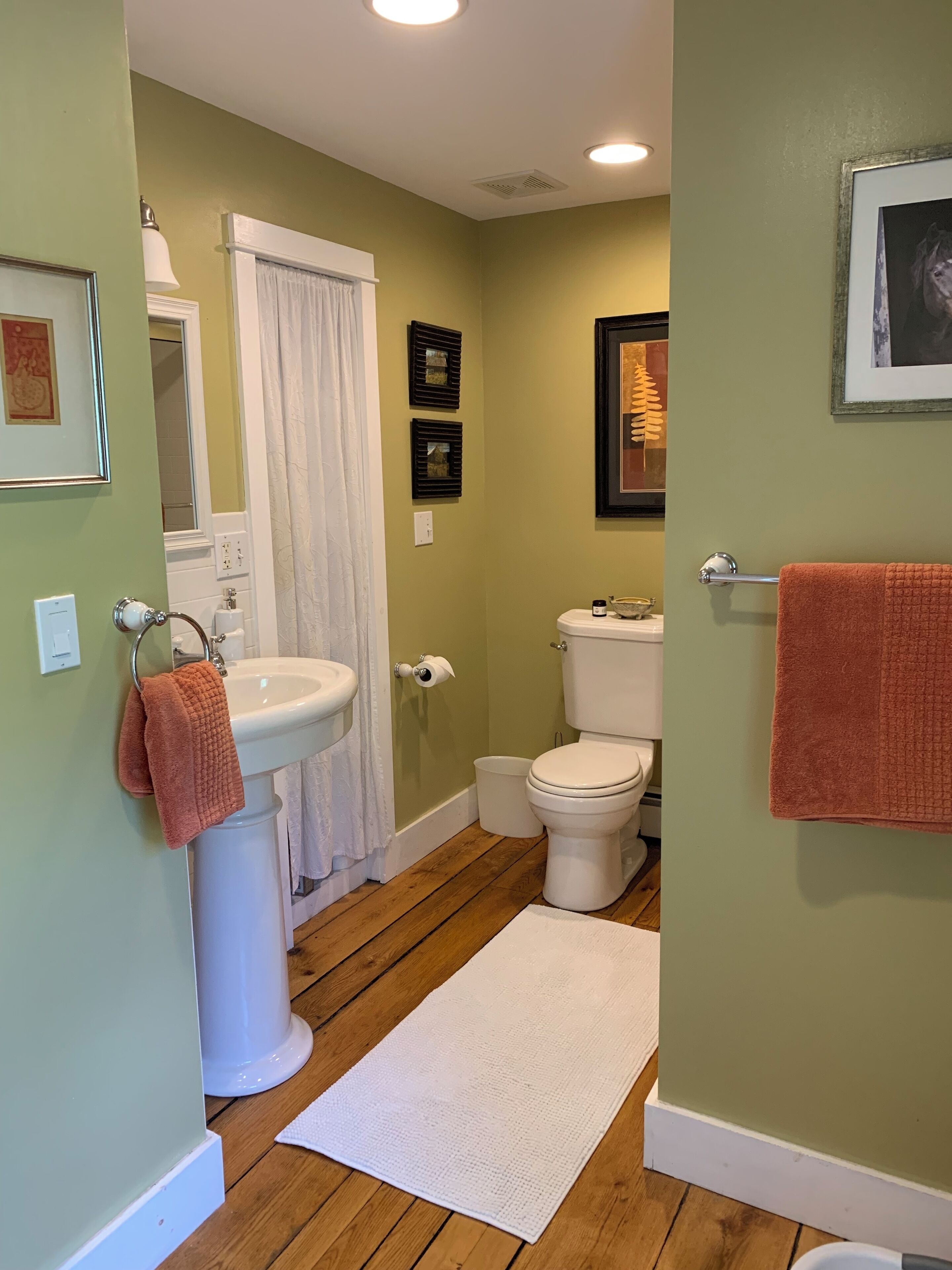 A bathroom with a white sink, toilet, and shower curtain. There are towels hanging on the wall and a white rug on the floor.