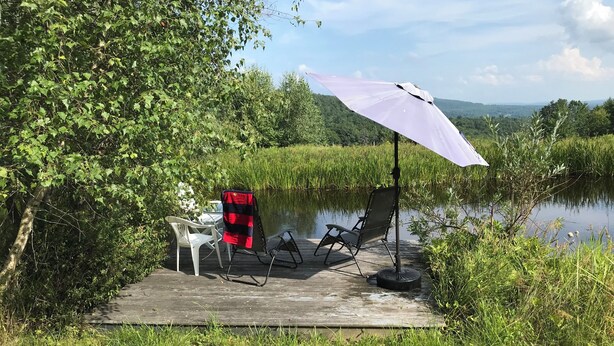 En træbro med et bord og stole, en lilla parasol og en stol med rødt og sort betræk.