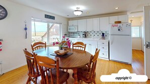 A dining area with a wooden table and chairs, a view of the outside, and a kitchen with white cabinets and appliances. - Margarita's at Seaside Beach (Seaside)