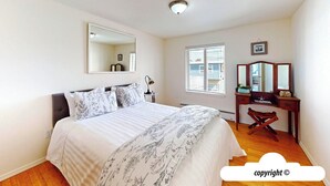 A bedroom with a bed, a desk, a chair, a mirror, and a window. - Margarita's at Seaside Beach (Seaside)