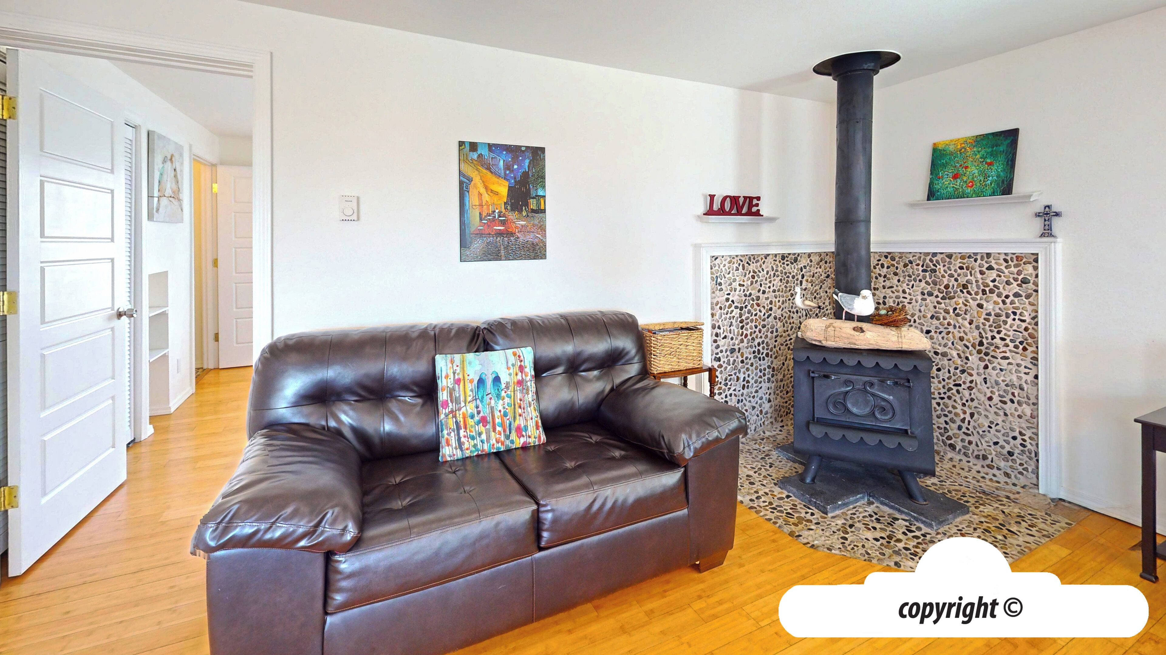 A living room with a brown leather sofa, a fireplace with a stone surround, and artwork on the walls.