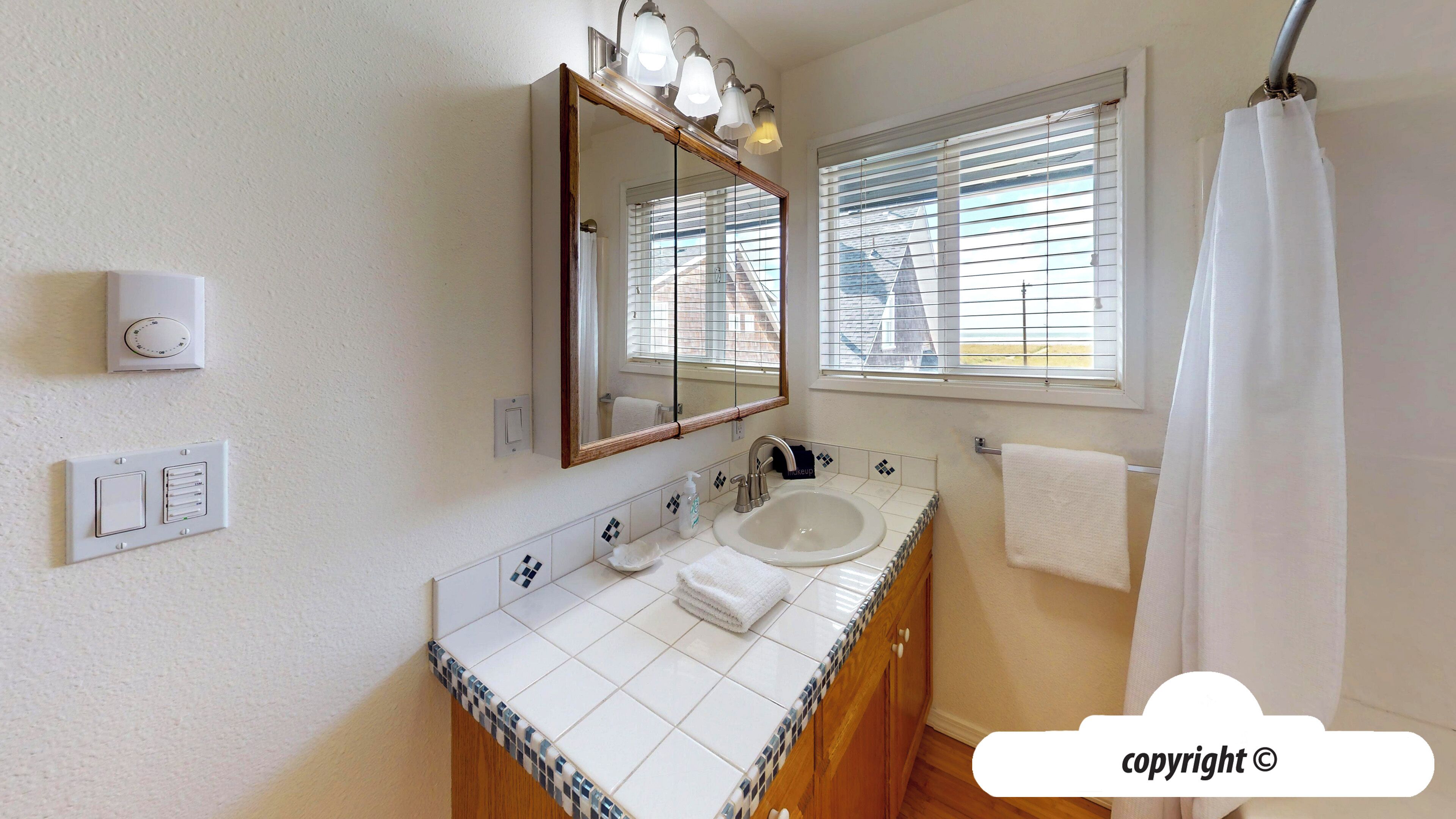 Een badkamer met een wastafel, spiegel en raam met zonwering.