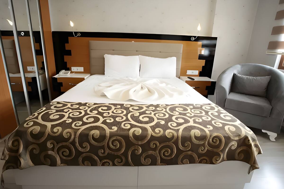 A modern hotel room with a large bed, a grey armchair, and a wooden headboard.