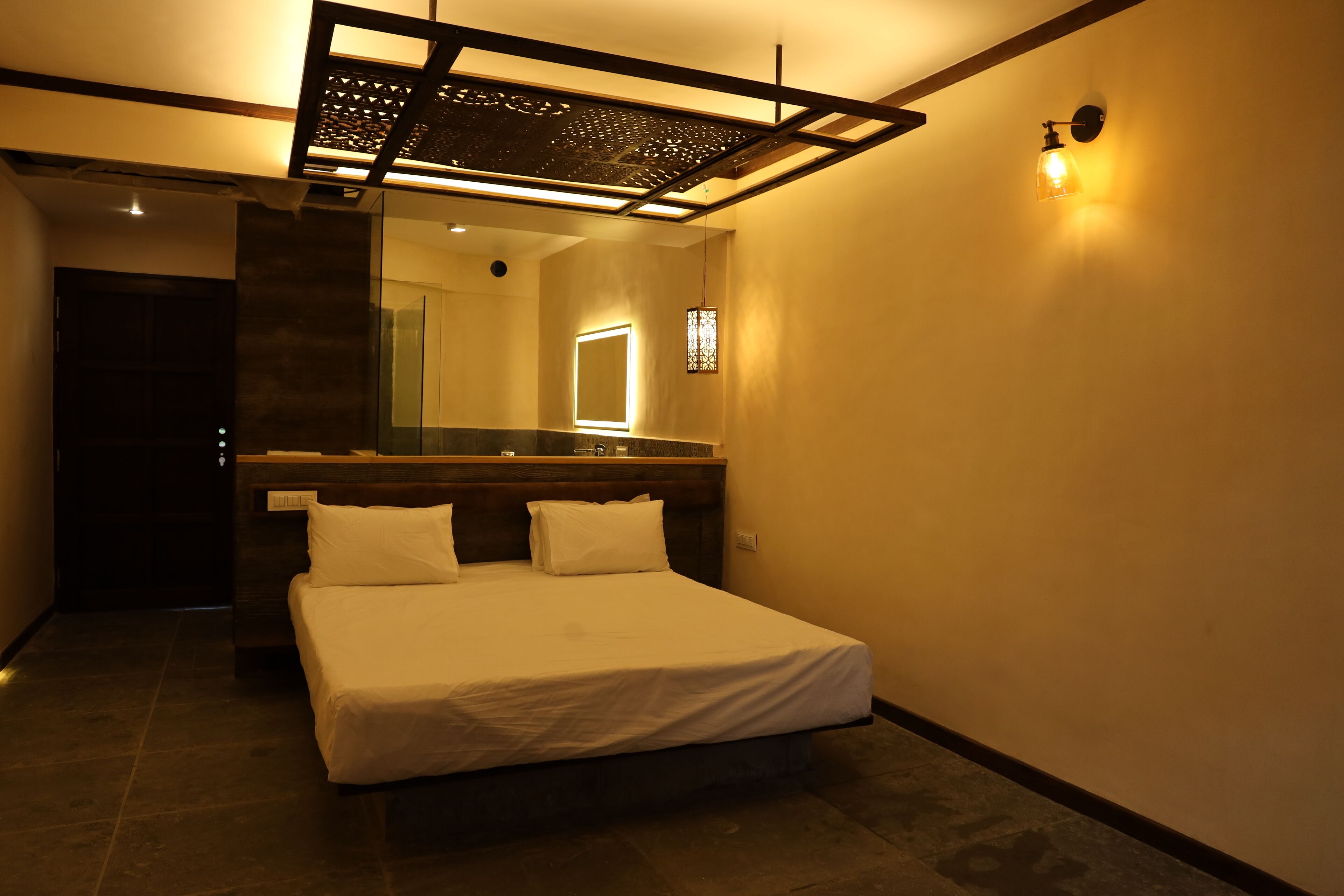 A hotel room with a bed, a large mirror, and a modern light fixture.