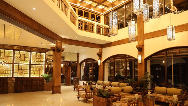 A spacious lobby with high ceilings, wooden columns, and a variety of seating arrangements. - Avhyay Resort (Vasai)