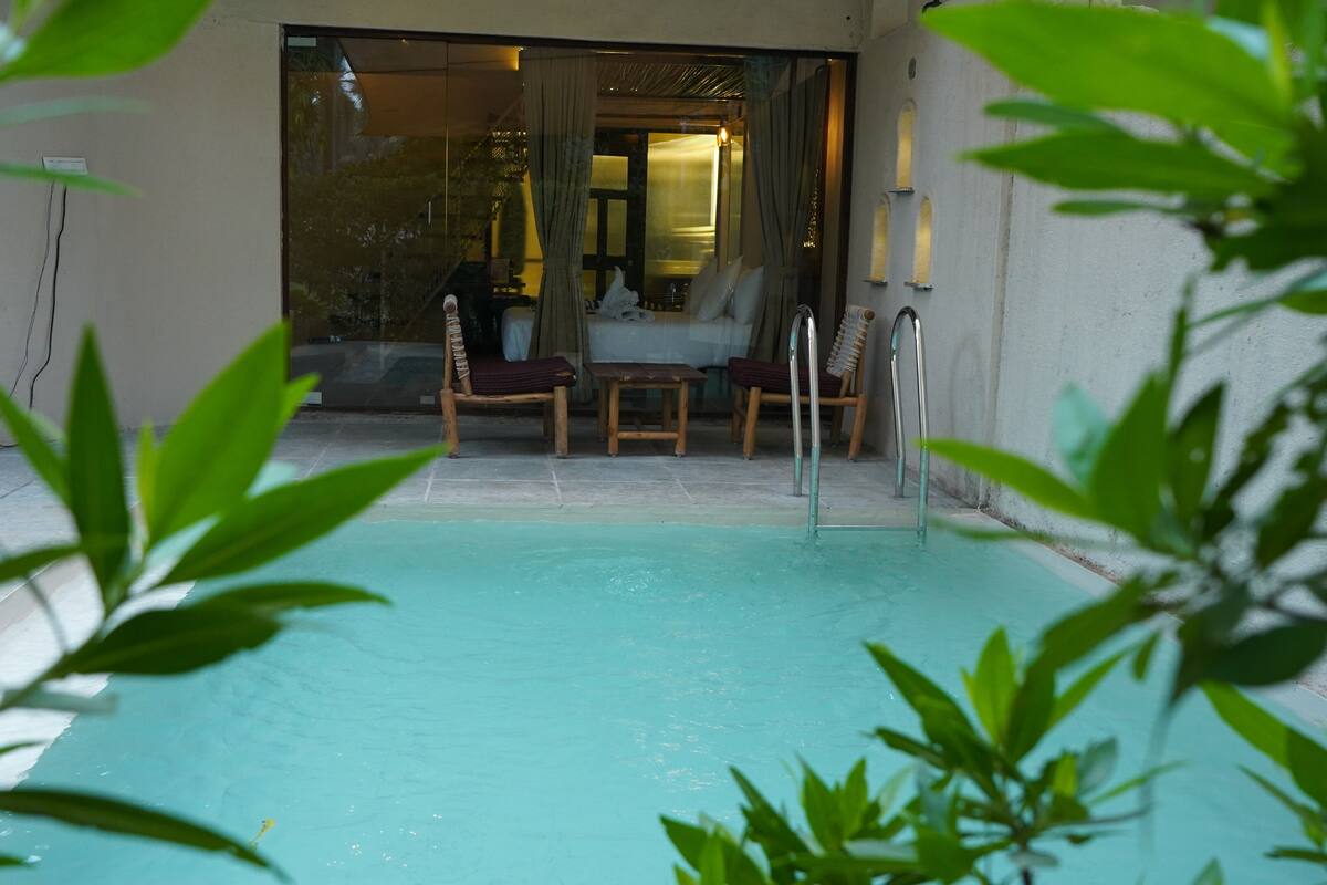 Une piscine intérieure à l’eau claire, entourée d’un sol carrelé et de chaises en bois.