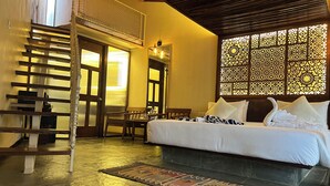 A hotel room with a bed, a wooden chair, a small table, and a decorative wall panel. - Avhyay Resort (Vasai)