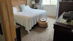 Quarto com cama, abajur, penteadeira e janela com cortinas.