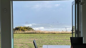 A view from a room with a door leading to a grassy area with a view of the ocean and distant islands. - Relax at "Rocky Point" - a private, modern home w/cliff views of the Tasman Sea. (Cape Foulwind)