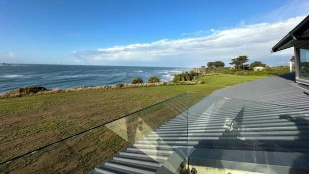 A modern building with a glass balcony overlooking a coastal landscape. - Relax at "Rocky Point" - a private, modern home w/cliff views of the Tasman Sea. (Cape Foulwind)