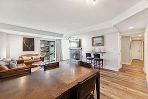 A spacious living area with a large wooden dining table, leather sofas, a fireplace, and a large window.