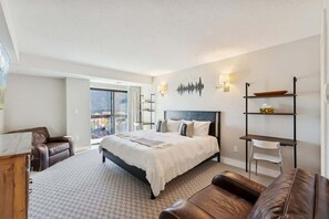 A bedroom with a large bed, a sofa, a desk, and a chair. There is a window with a view of the outside.