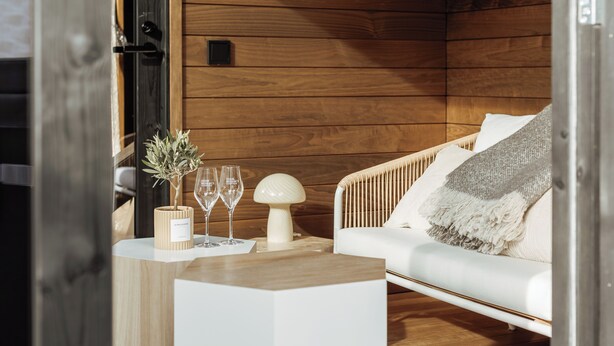 A cozy room with wooden walls, a white sofa, a small table with a plant, two glasses, and a decorative lamp. - l'empreinte  (Verzenay)